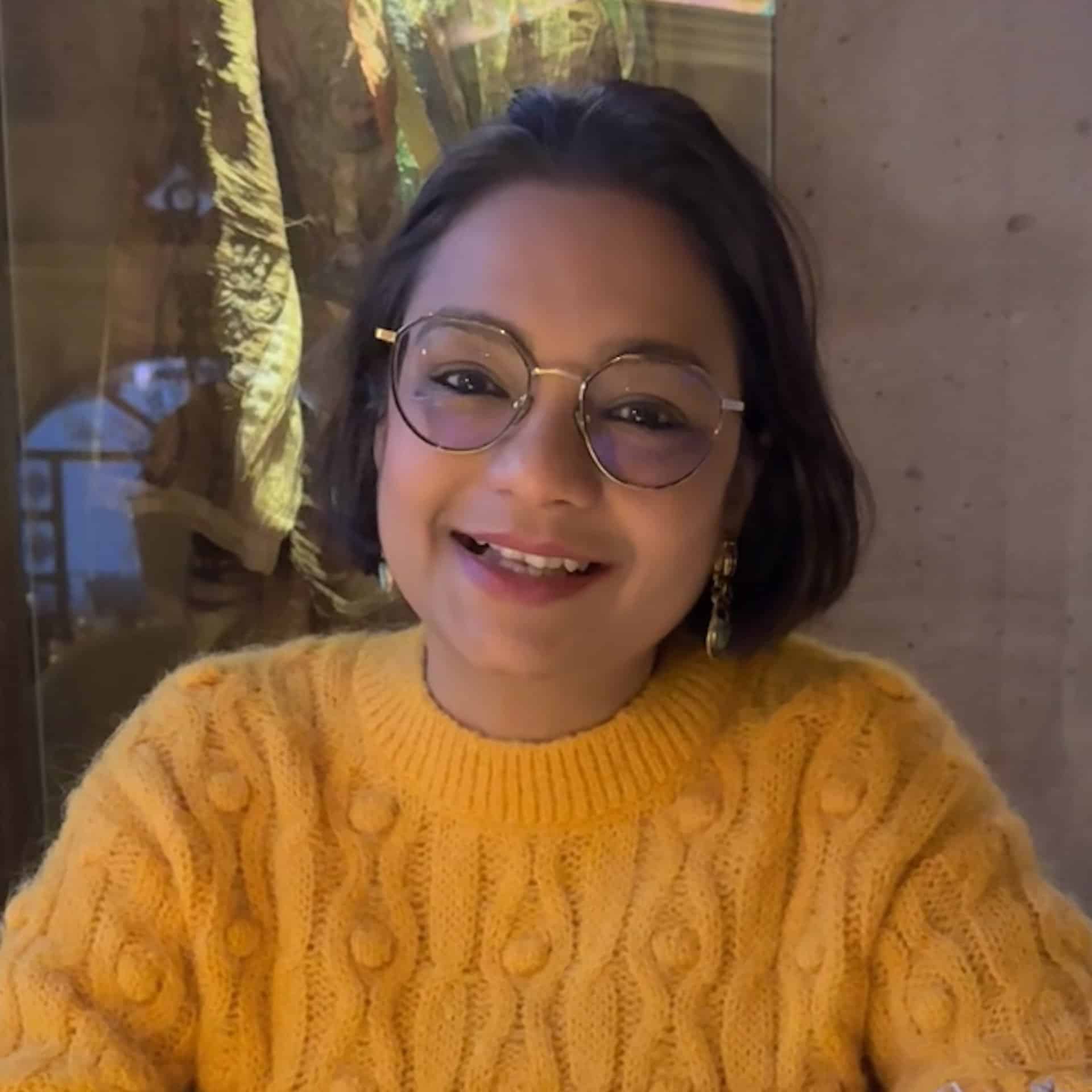 A headshot of Monal Sanghvi wearing a orange jumper.