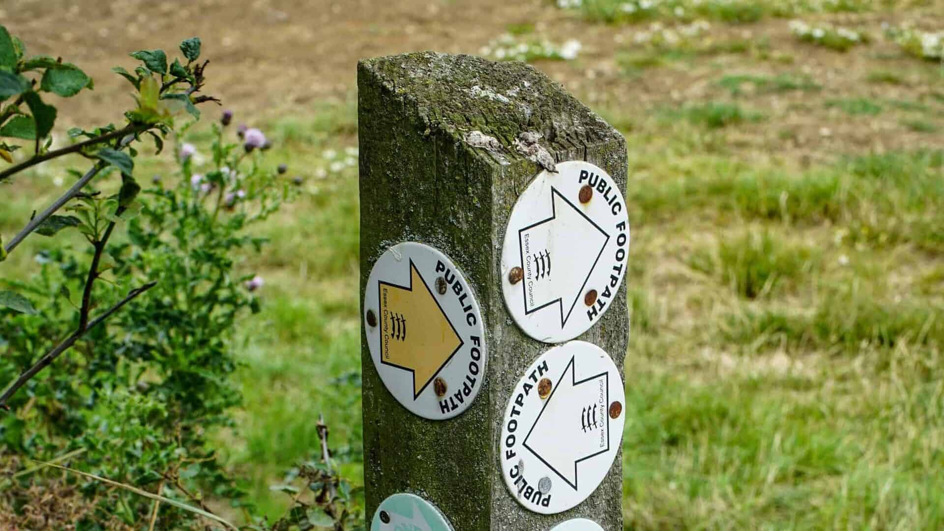 A wooden signpost with multiple badges on it, each of which point in different directions to different locations.