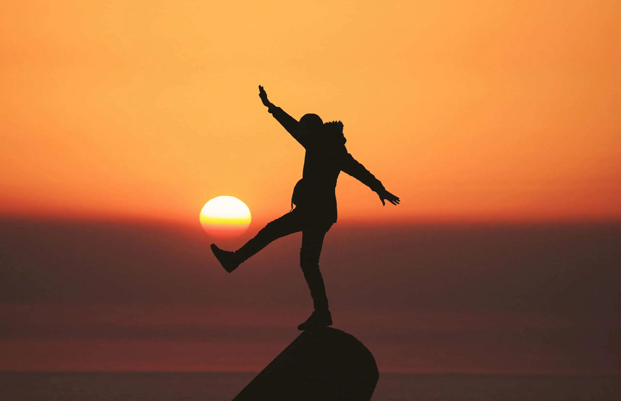 A portrait of a person balancing on one foot on a rock during sunset.