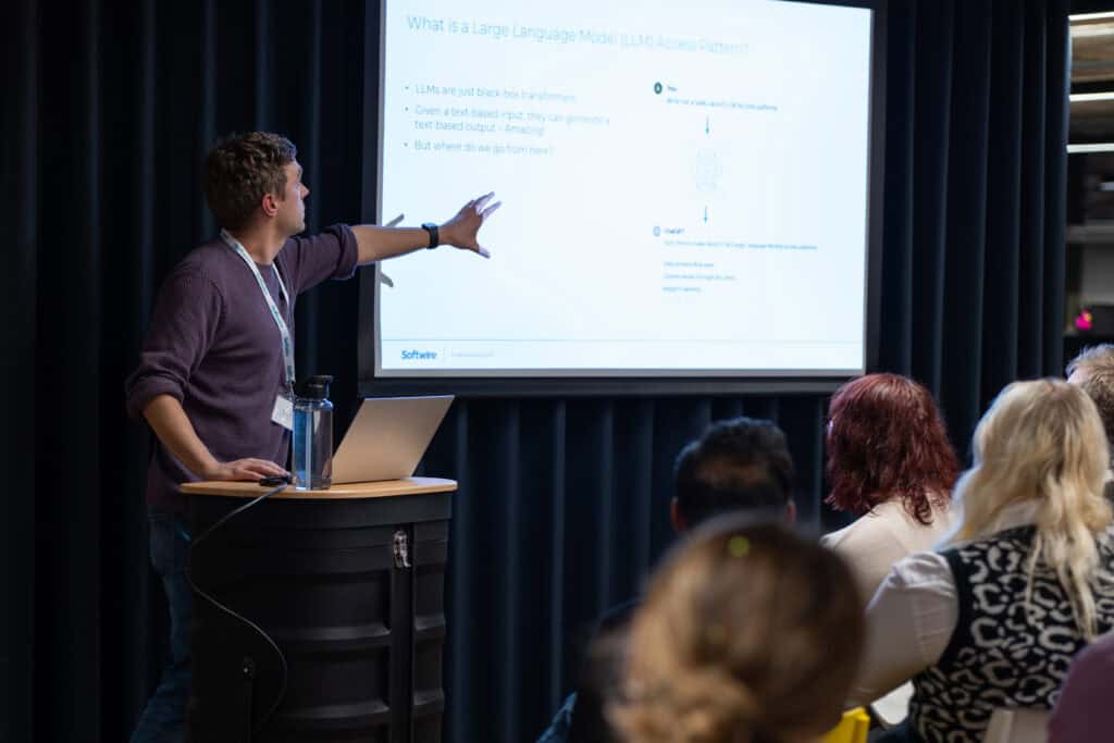 Anthony Pengelly from Softwire speaking at latern in front of a crowd. He is pointing at a presentation behind him. 