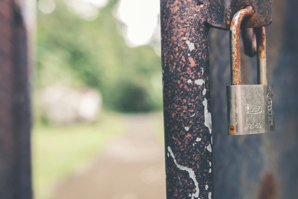 A picture of a gate post with lock on it and the gate ajar.