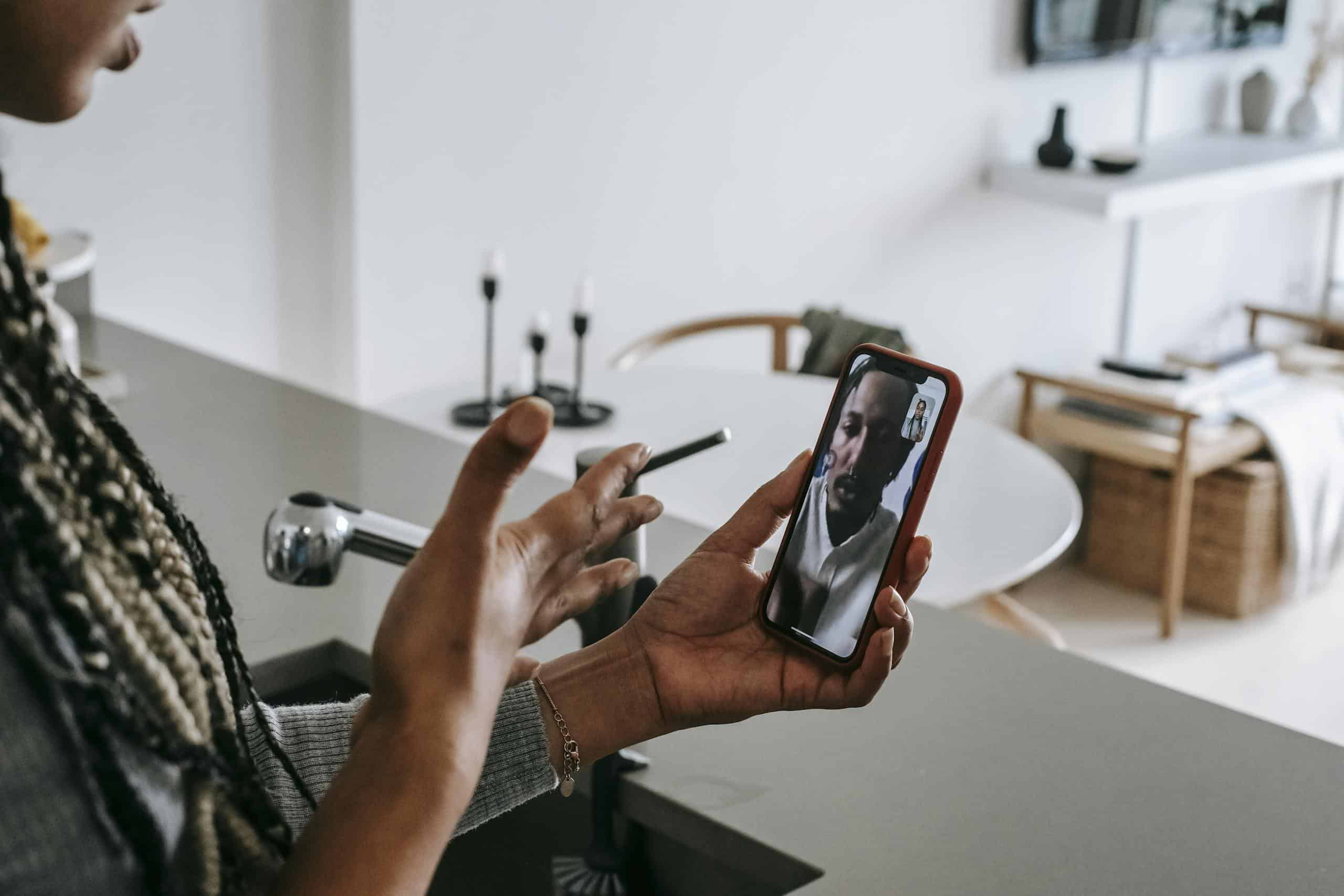 High angle of crop unrecognizable young black female gesticulating while having video conversation on smartphone with boyfriend in kitchen