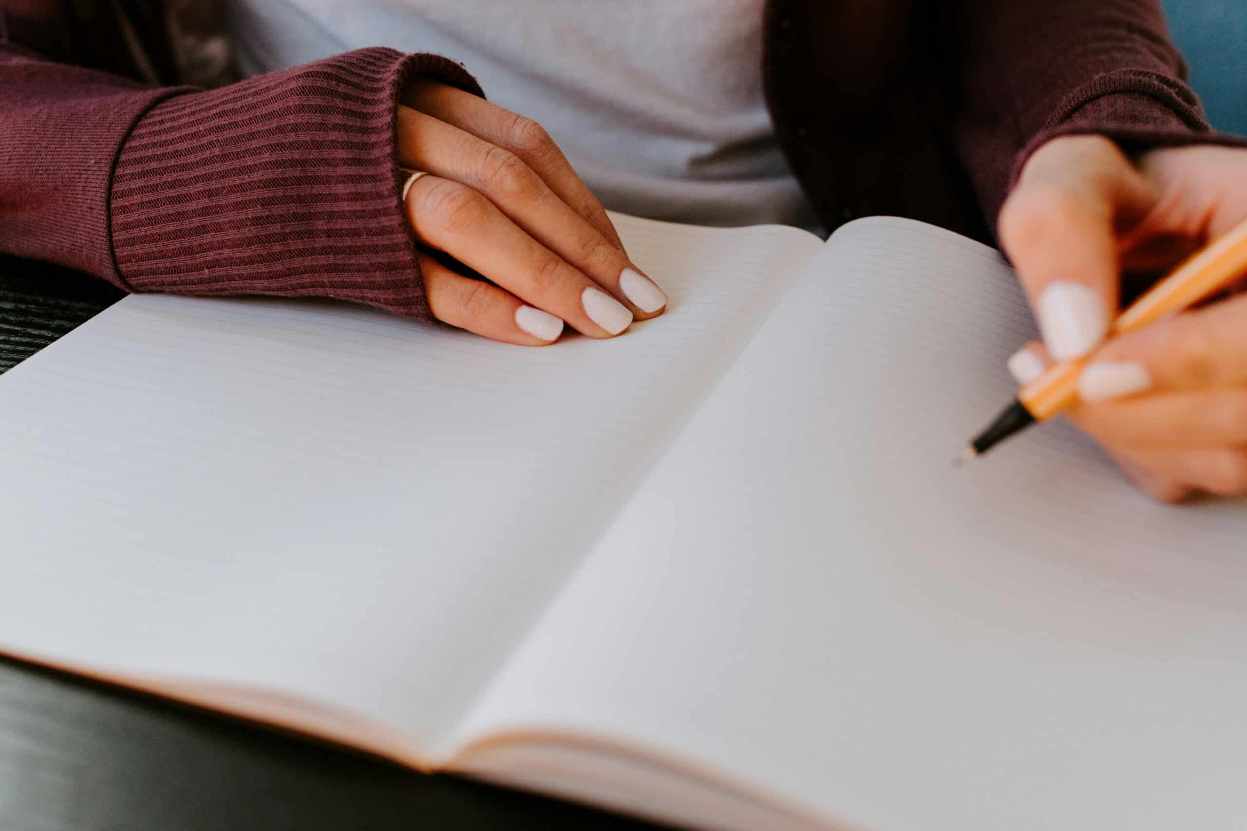 A close up of a person's hands as they write they begin to write in an empty notebook.